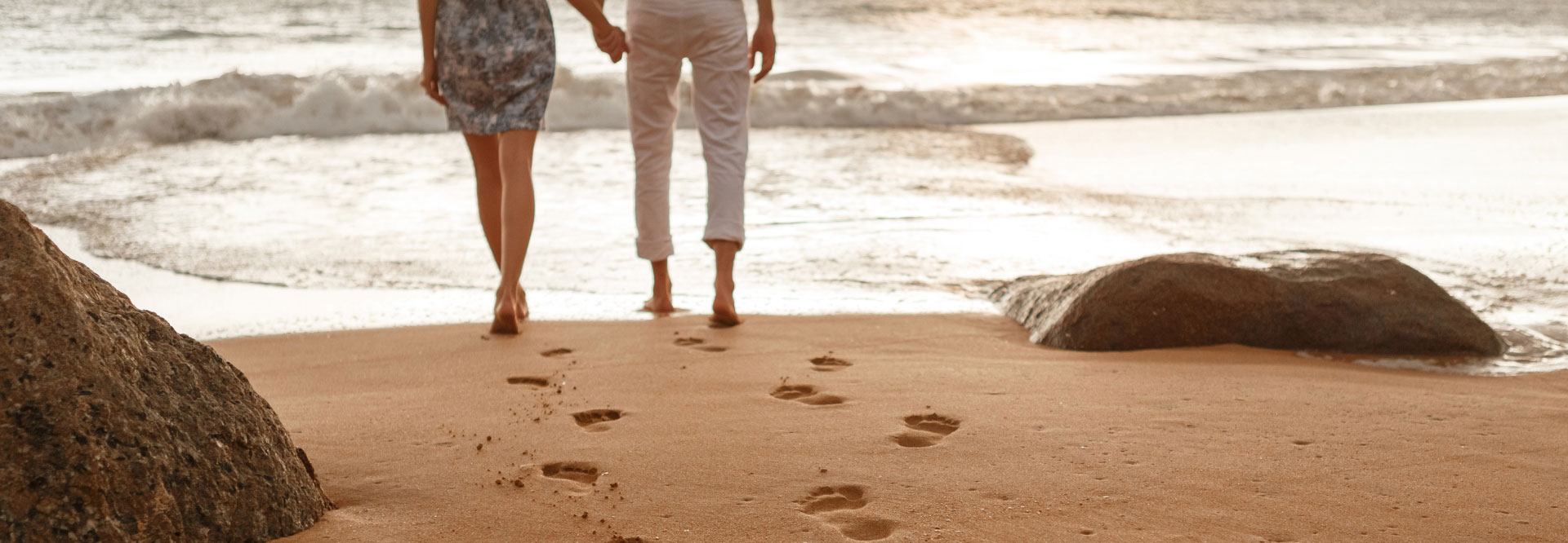 Couple walking on beach with footprints in sand