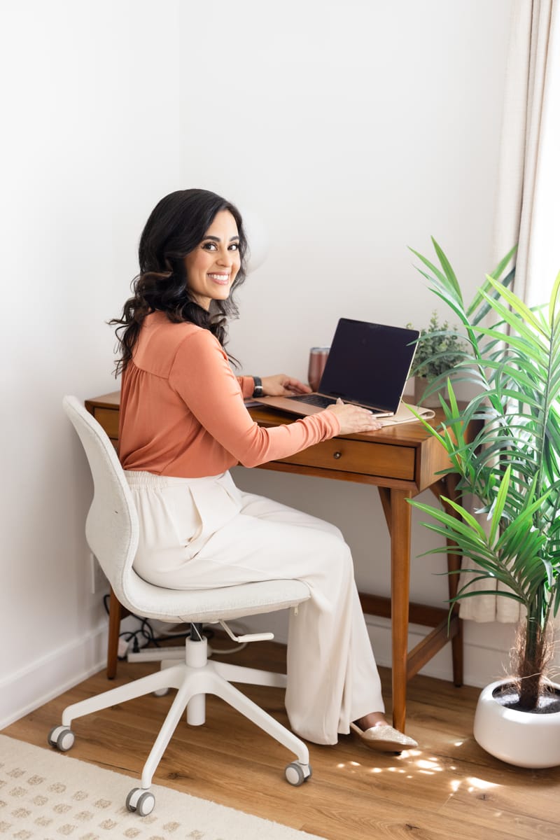 A therapist sits at a desk, with a MacBook.