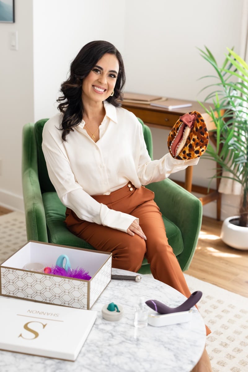 Dr. Shannon Chavez is seated on a green velvet chair, with a box in front of her containing various toys and instruments utilized in couples therapy.