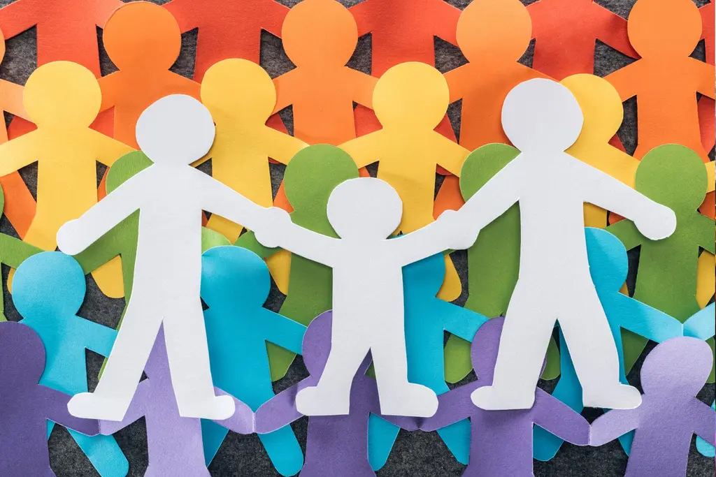 Colorful paper cutout figures forming a rainbow backdrop behind a white paper family holding hands, symbolizing LGBTQ+ family inclusion, unity, and diversity.