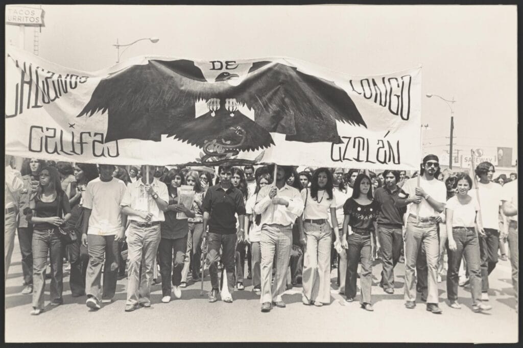 Chicano protesters holding signs and banners during a civil rights demonstration, advocating for equality and cultural pride