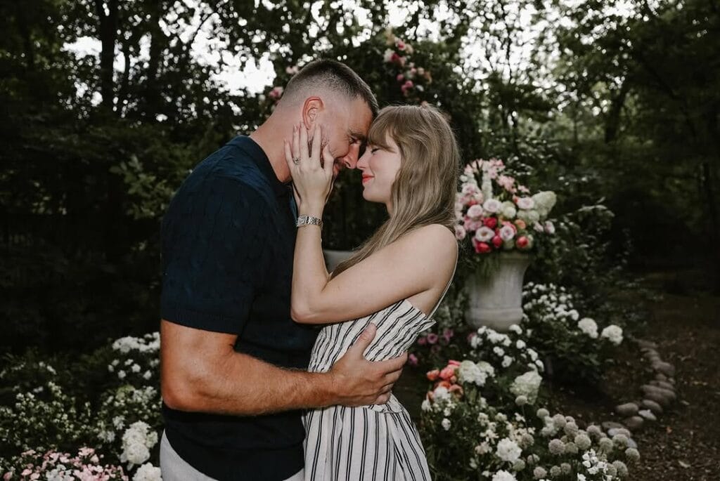 Taylor Swift and Travis Kelce share a close embrace in a romantic garden setting after their engagement, surrounded by flowers and natural light.”