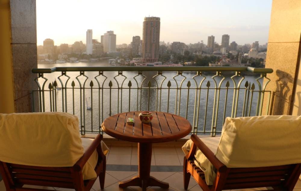 Sunset view over the Nile River from a Cairo balcony, with two chairs and a small table overlooking the water.