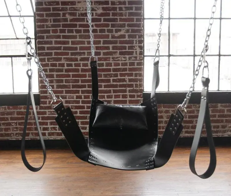 A black leather sling from Stockroom.com, suspended by chains for supported positioning and body exploration.