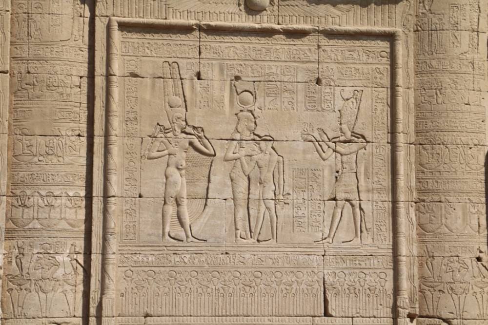 Relief carving of Osiris, Isis, and Horus with a pharaoh making offerings, symbolizing resurrection, divine union, and continuity in ancient Egyptian belief.