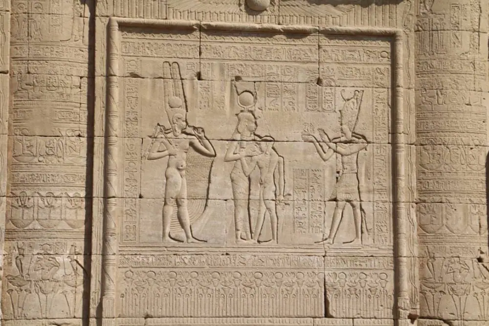 Relief carving of Osiris, Isis, and Horus with a pharaoh making offerings, symbolizing resurrection, divine union, and continuity in ancient Egyptian belief.