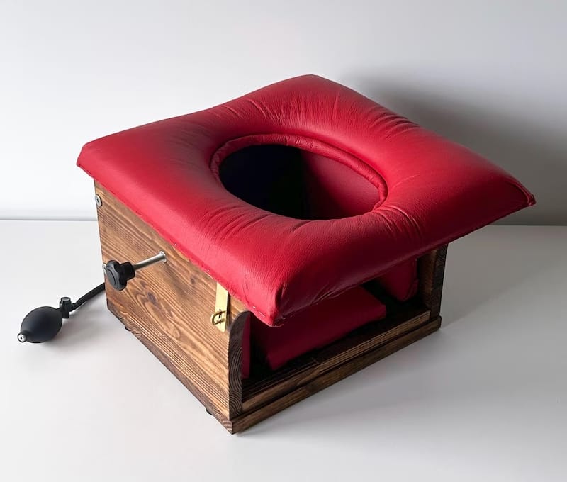 Vintage-style wooden queening chair with padded red leather seat and central opening for facesitting.