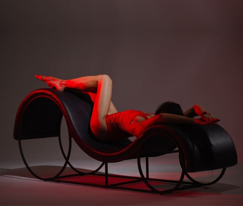 A curvaceous S-shaped tantra chair upholstered in black leather, designed for comfort and erotic positioning.