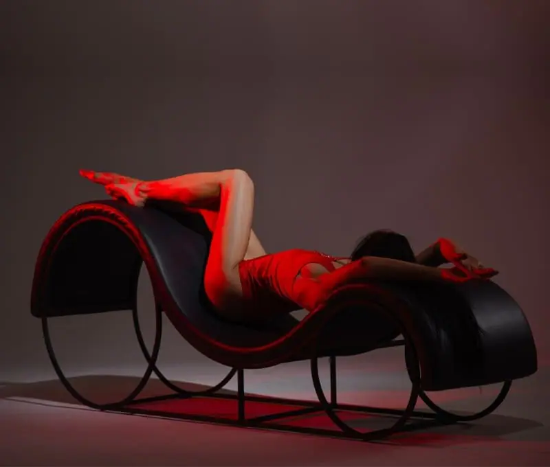 A curvaceous S-shaped tantra chair upholstered in black leather, designed for comfort and erotic positioning.