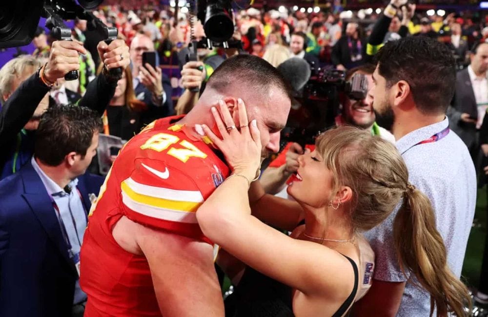 Taylor Swift embraces Travis Kelce on the football field after the Kansas City Chiefs’ victory, capturing the classic ‘popular girl and football star’ love story that fans adore.