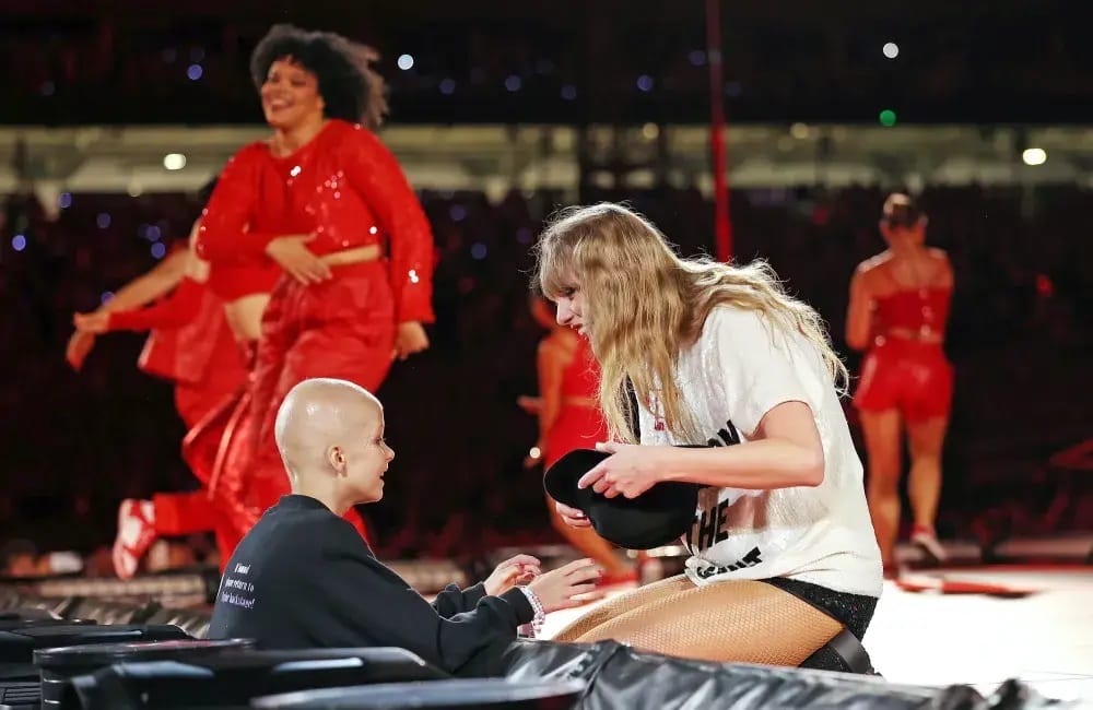 Taylor Swift kneels on stage giving her ‘22’ hat to nine-year-old fan Scarlett Oliver during the Eras Tour in Sydney, creating a heartfelt moment of connection.