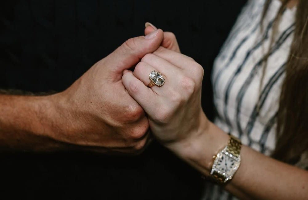 Close-up of Taylor Swift and Travis Kelce holding hands, showing her engagement ring.